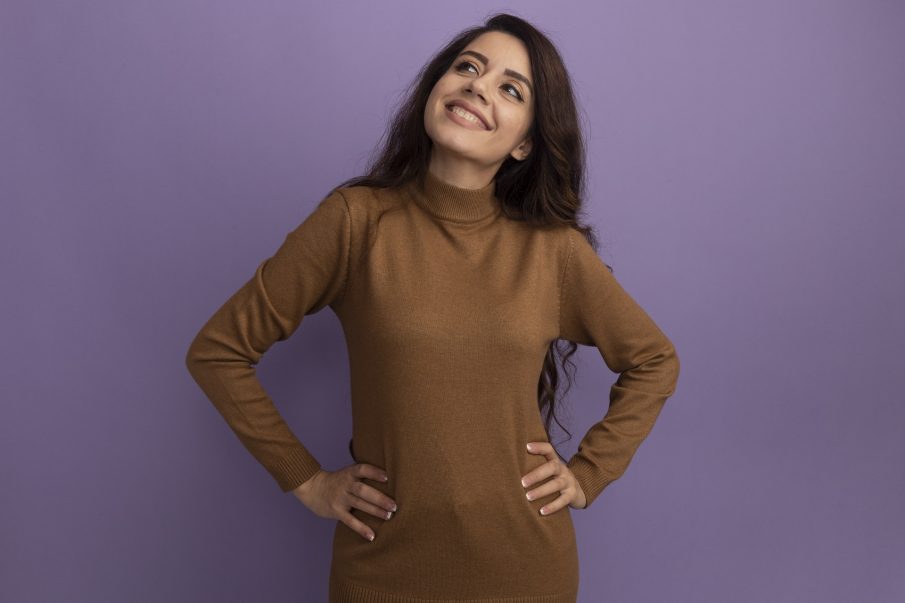 smiling-looking-side-young-beautiful-girl-wearing-brown-turtleneck-sweater-putting-hands-hip-isolated-purple-wall-1.jpg